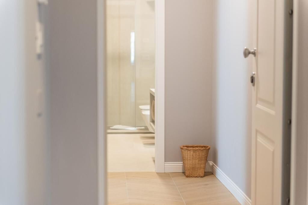 Un pasillo estrecho con una cesta de mimbre en el suelo, que conduce a un baño con inodoro y lavamanos.