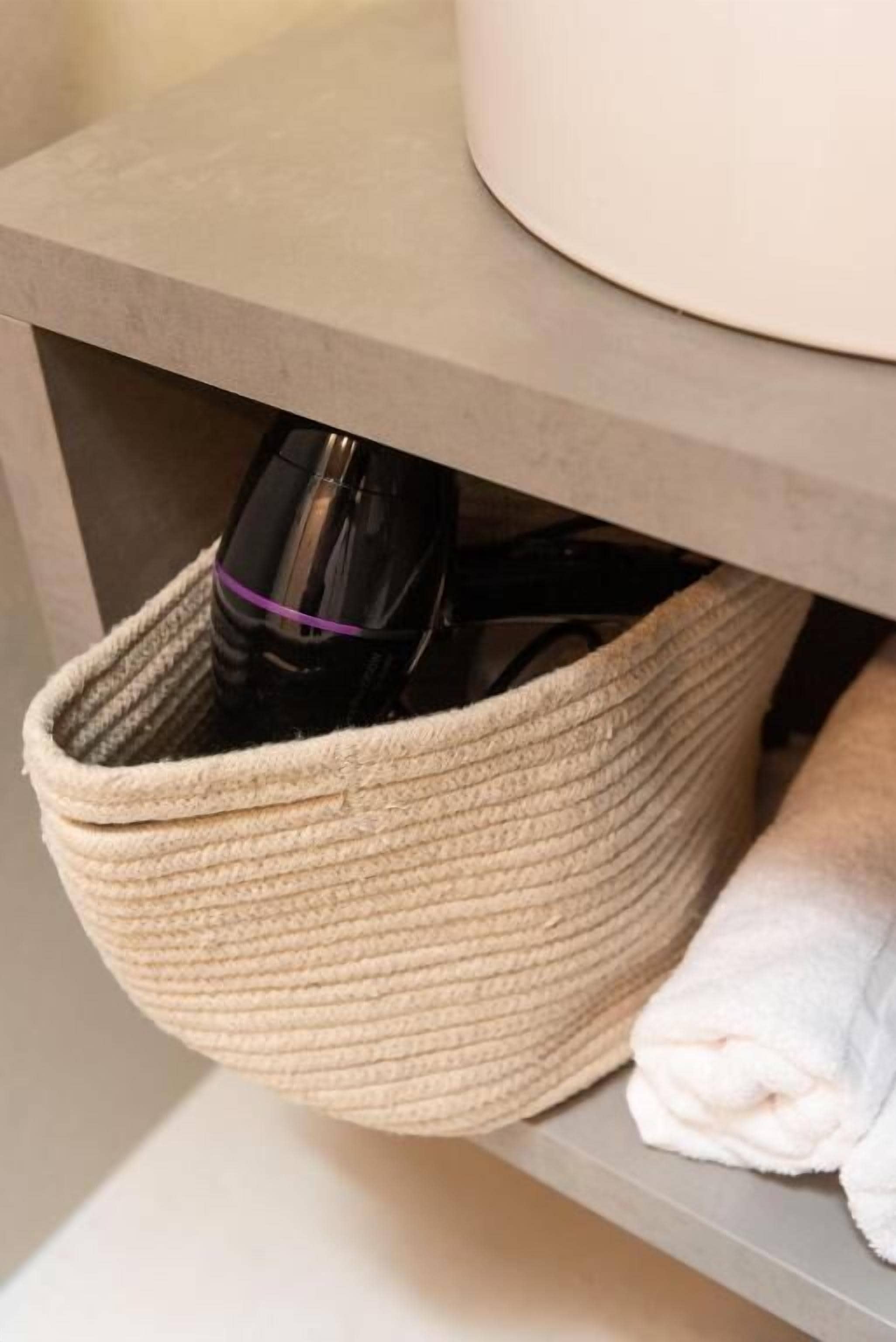 A woven basket under a shelf containing a black bottle and a rolled-up white towel.