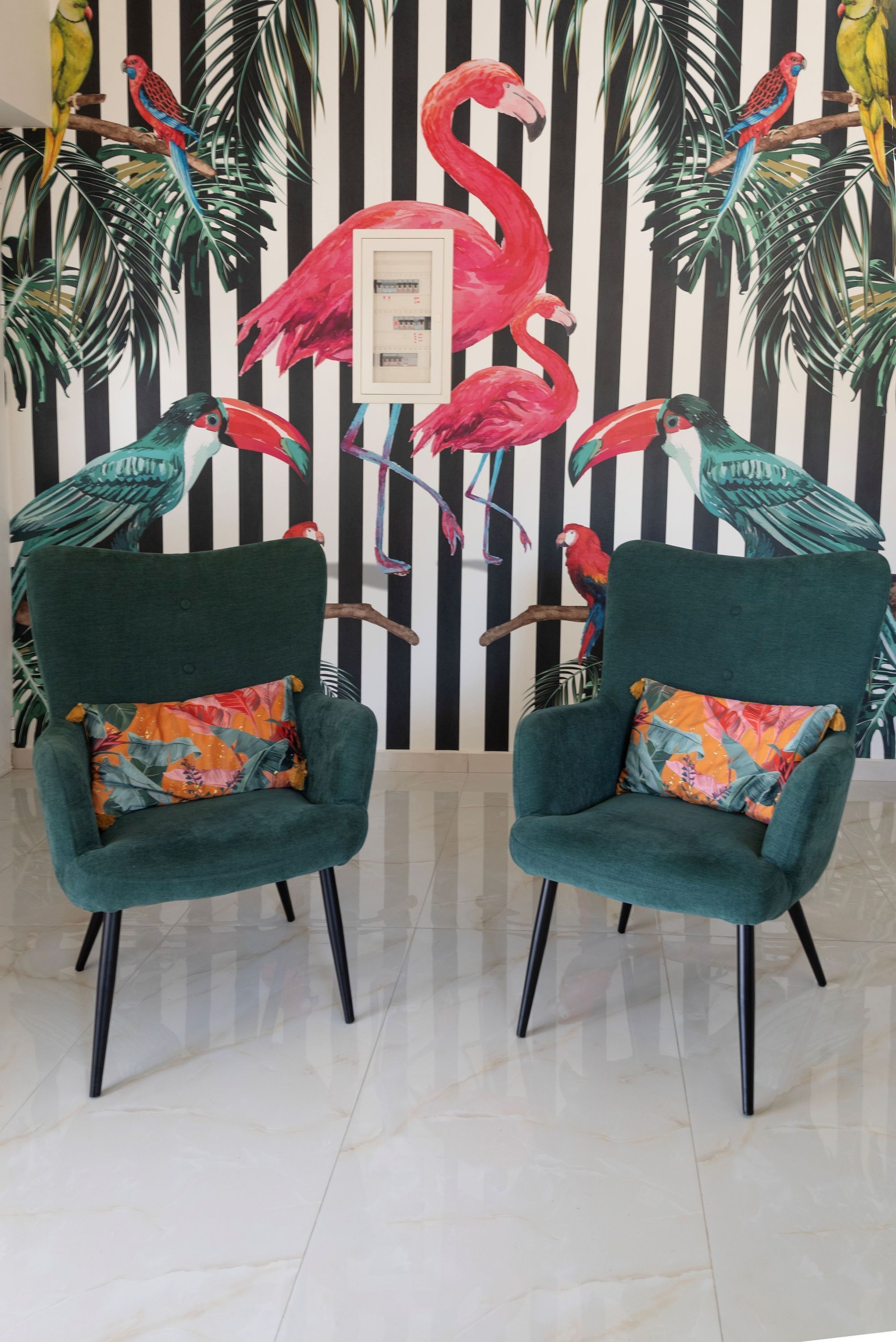 Dos sillones turquesa con cojines coloridos, frente a una pared con un mural tropical que muestra aves y flamencos.