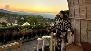 Eine Person steht auf einem Balkon und blickt auf einen Berg und einen Sonnenuntergang.
