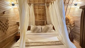 Ein Zimmer mit Holzboden, einem Bett mit weißer Bettwäsche und einem Baldachin.