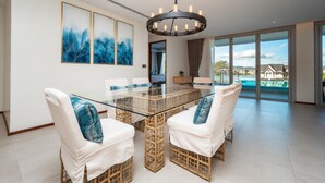 Uma sala de jantar moderna com mesa de vidro, cadeiras de vime e um candelabro.
