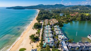 Vista aérea de um resort costeiro com villas na praia, uma praia de areia e um lago.