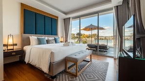 Quarto de hotel moderno com uma cama grande, um banco, uma TV, uma varanda com vista para o mar e uma janela ampla.