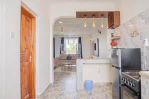 Cocina compacta con refrigerador, estufa y un pequeño comedor con mesa y sillas.