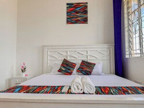Una cama bien hecha con dos almohadas, una manta colorida y dos toallas enrolladas.