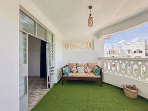 Un balcon avec un canapé, du gazon synthétique, un luminaire suspendu et une vue sur les immeubles.
