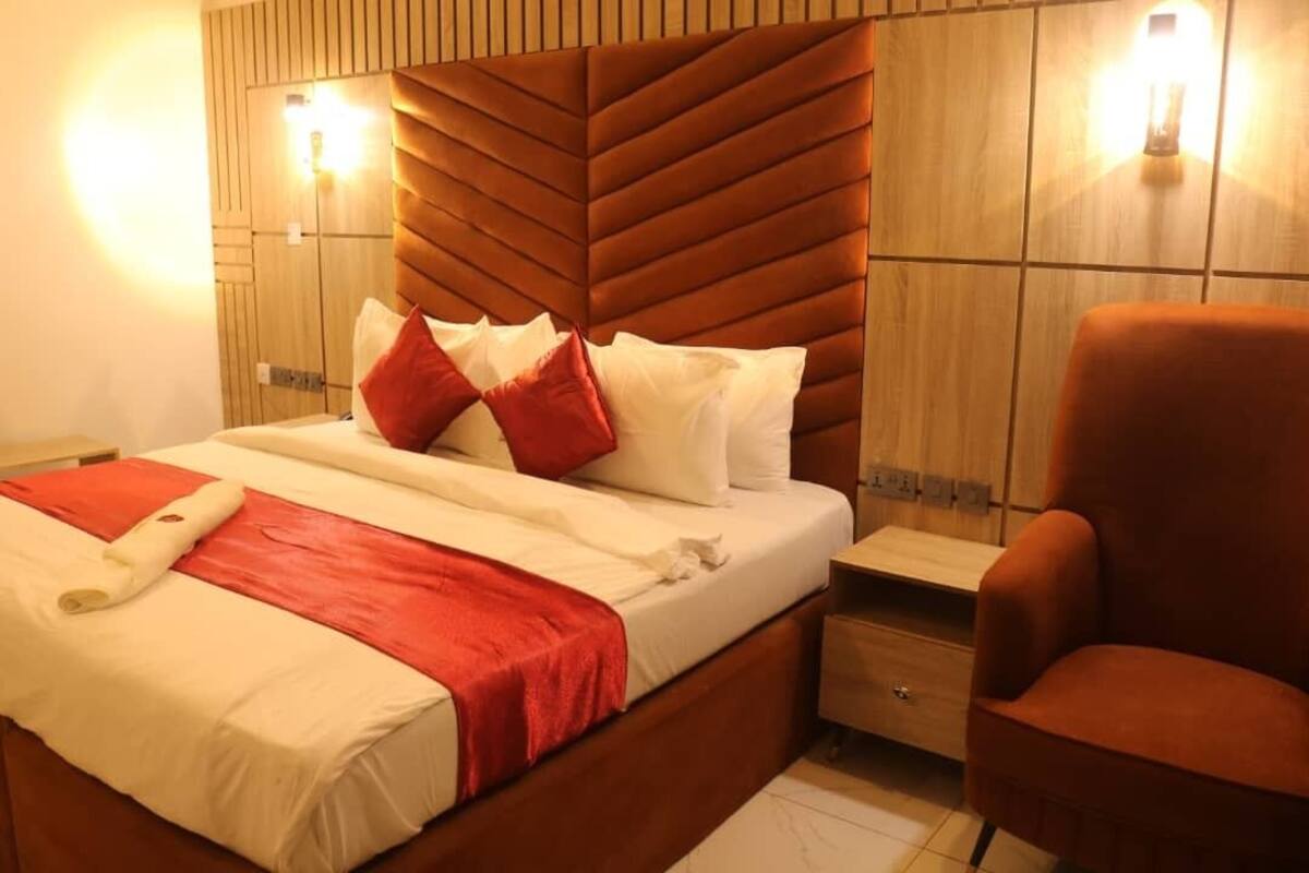 Ein Hotelzimmer mit einem großen Bett, einem hölzernen Kopfteil, zwei Nachttischlampen, einem roten Sessel und einem kleinen Nachttisch.