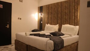 A neatly made bed with white and dark bedding, a wooden headboard, and a wall-mounted light fixture. - VICTORIAN BLOOM HOTEL AND RESORT (Asaba)