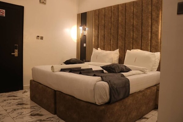 Una cama bien tendida con ropa de cama blanca y oscura, un cabecero de madera y una lámpara de pared.
