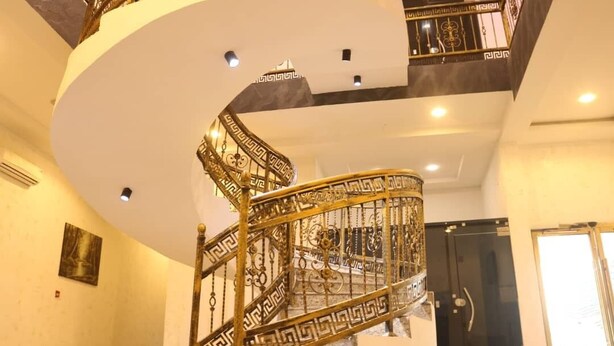 A spiral staircase with ornate golden railings and a black door at the top. - VICTORIAN BLOOM HOTEL AND RESORT (Asaba)