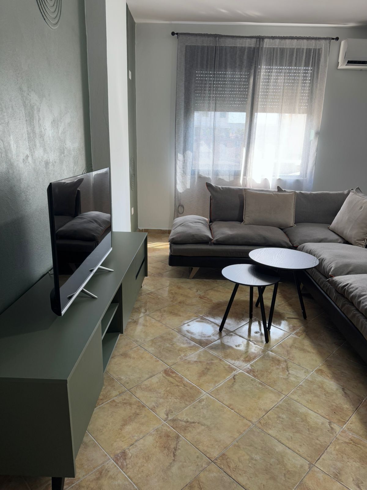 A modern living room with a sectional sofa, a flat-screen TV, and a small round table.