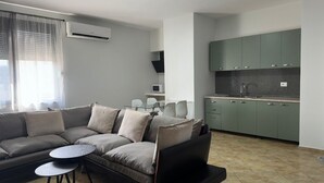 A modern living room with a sectional sofa, a small round table, and a kitchen area with green cabinets and a tiled backsplash. - Tirent Apartment-One Bedroom Central (Tirana)