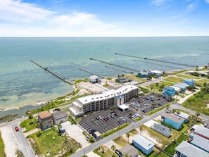 An aerial view of a coastal area with a large building, parking lot, and several piers extending into the water. - Tradewinds - Laguna Reef Waterfront Condo unit 305 (Rockport)