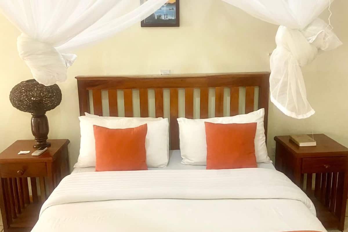 Cama com dossel branco, cabeceira de madeira e almofadas laranja.