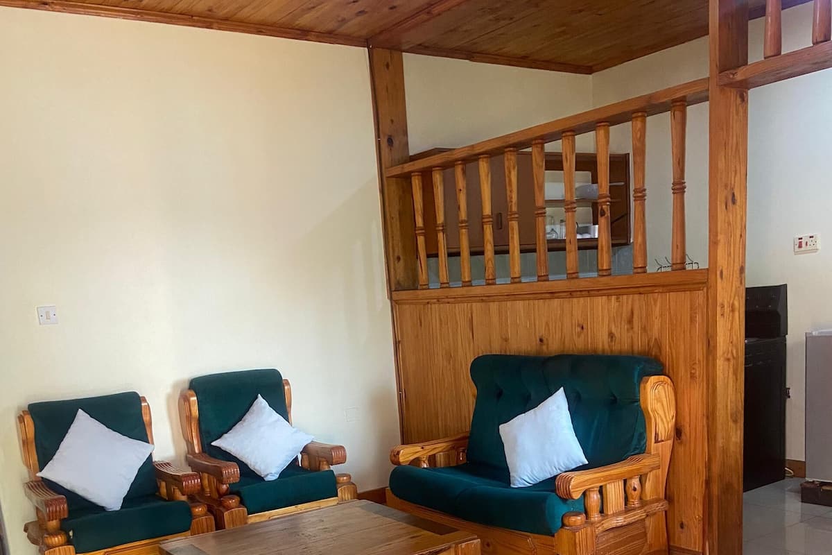 Um quarto com duas poltronas de madeira com almofadas verdes, uma mesa de centro de madeira e um tapete estampado com padrão de zebra.