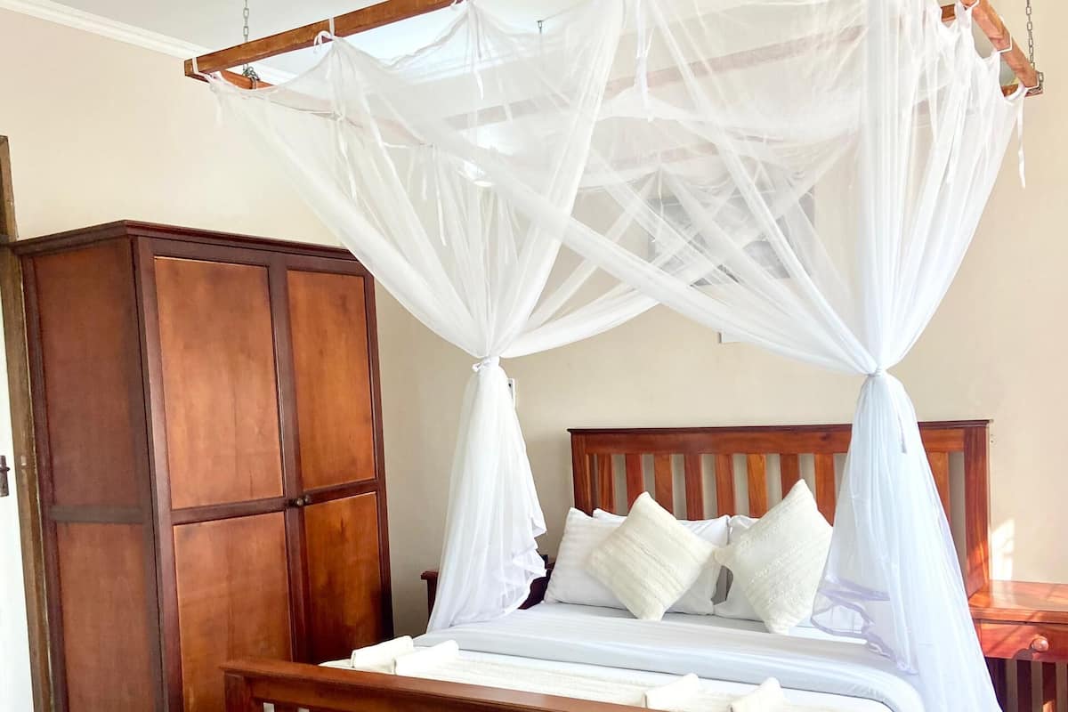 Uma cama de dossel com cortina, cabeceira de madeira e roupa de cama branca.