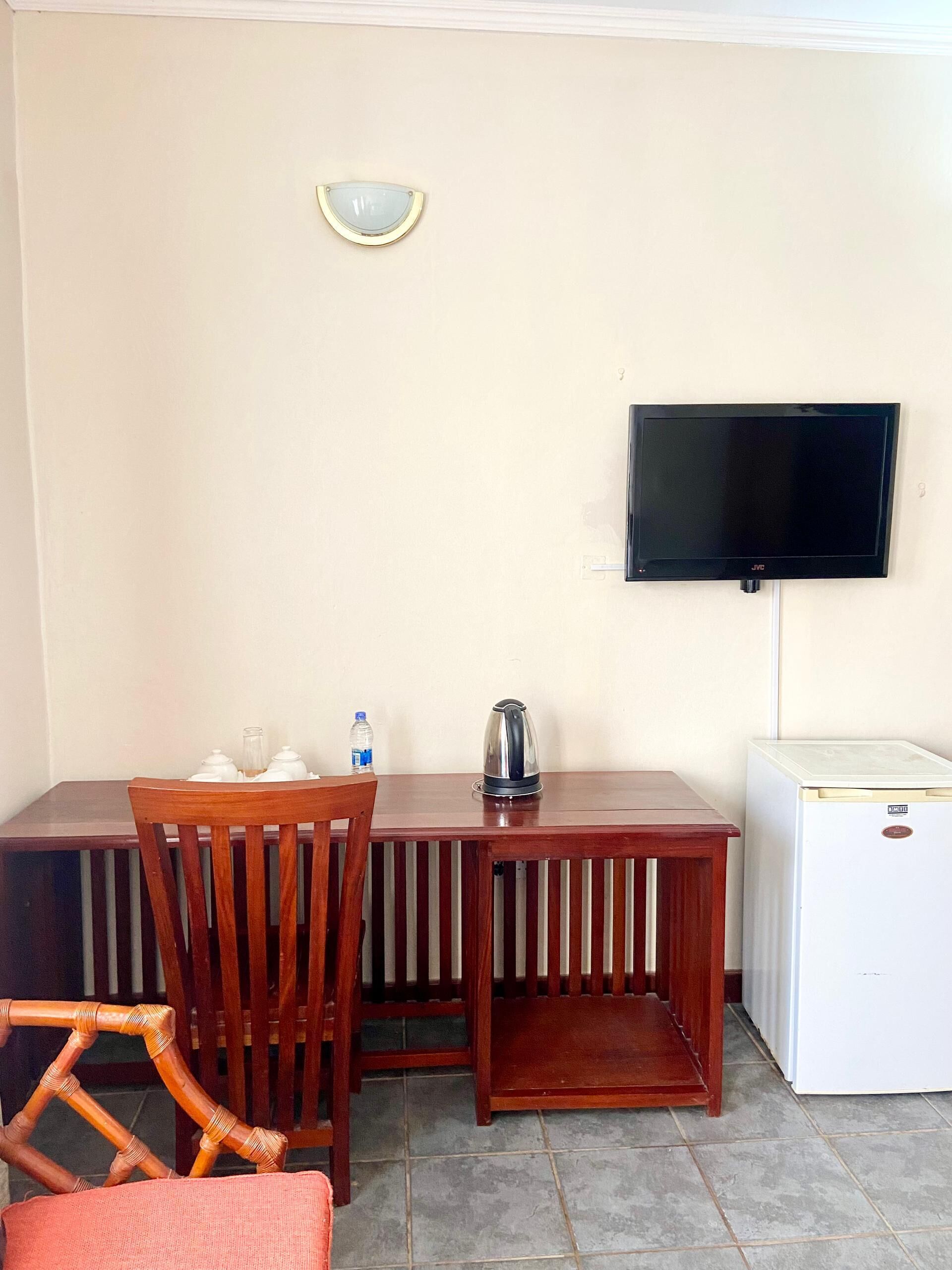 A dining area with a table, chairs, a television, a kettle, and a refrigerator.