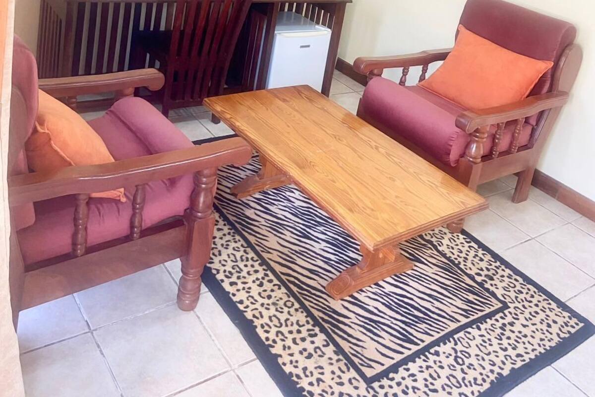 Uma sala de jantar com mesa de madeira, duas cadeiras, um frigorífico pequeno e um tapete com padrão de zebra.