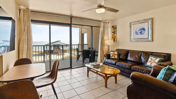 A spacious living area with a balcony, a leather sofa, a coffee table, and a dining table. - Paradise | Waterfront Comfort at Laguna Reef 411 (Rockport)