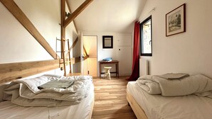 Ein Zimmer mit zwei Betten, Holzbalken, einem Schreibtisch und einem Fenster mit rotem Vorhang.