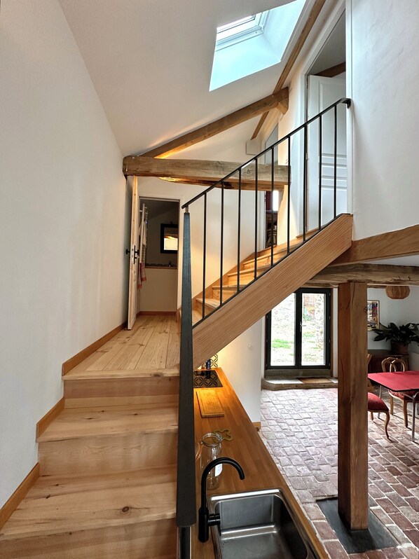 A wooden staircase with a metal railing leading to an upper floor. A skylight above the staircase allows natural light to enter.