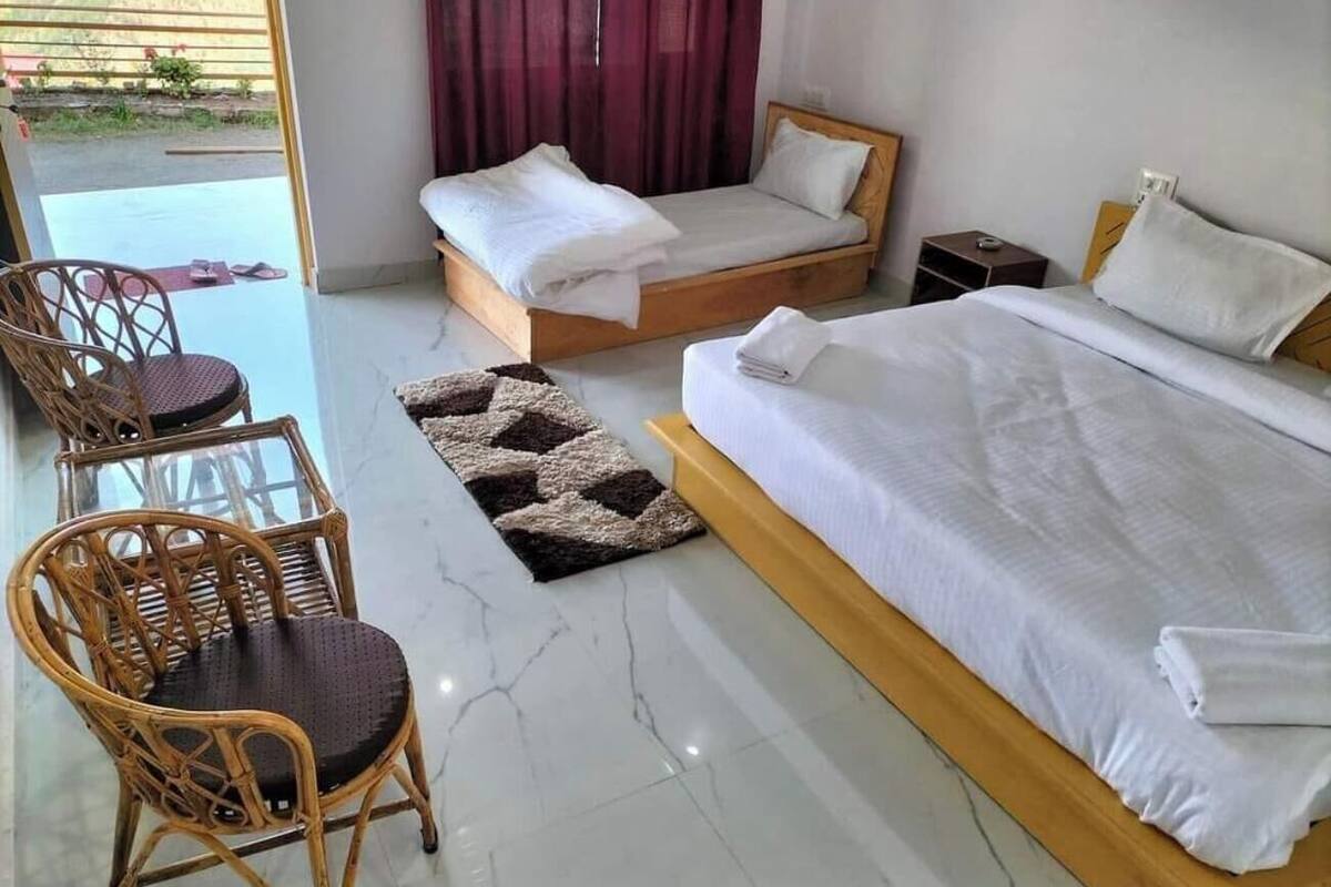 A hotel room with a large bed, two smaller beds, wicker chairs, a small table, and a view of the outdoors.