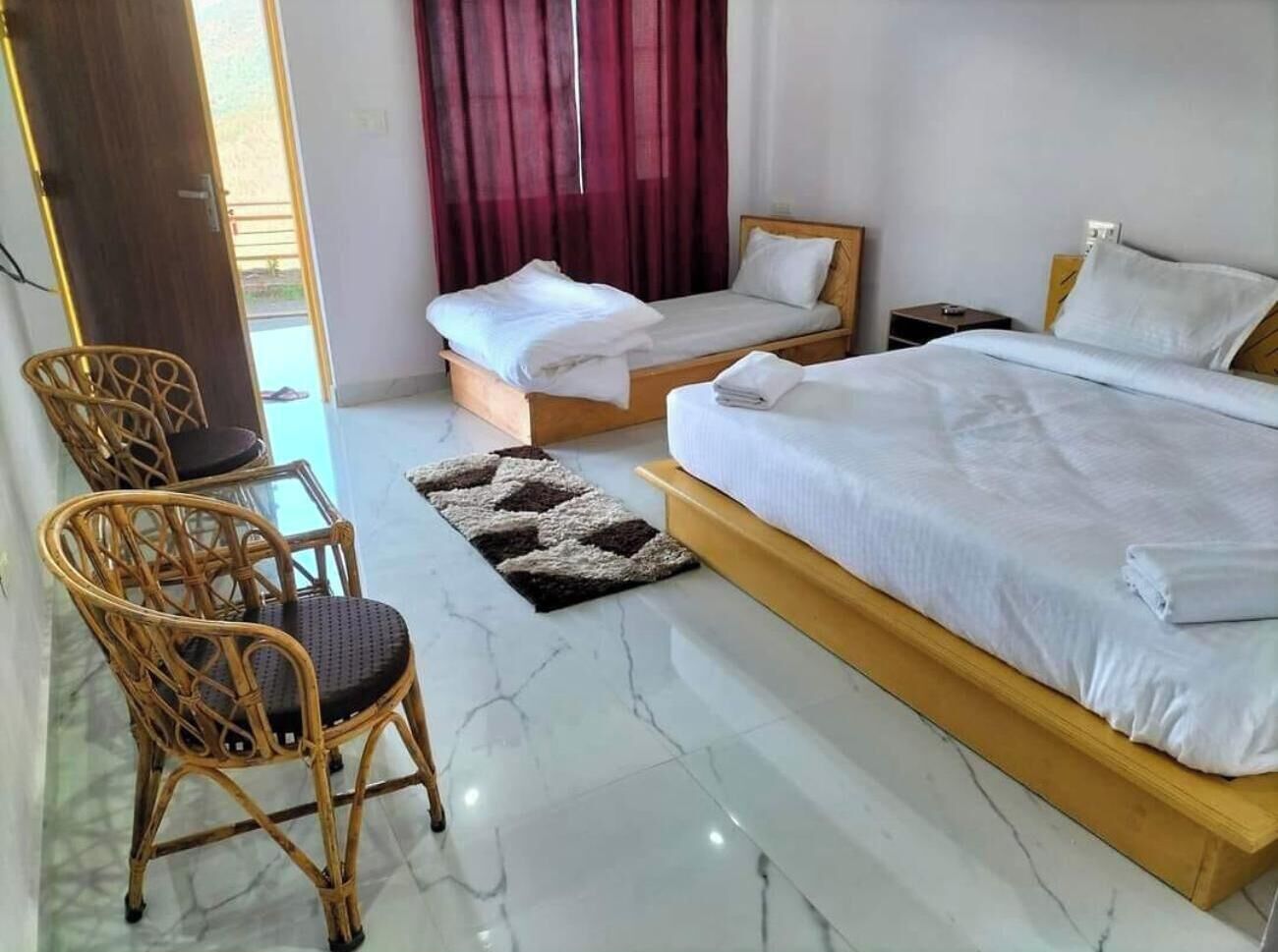 A hotel room with two single beds, a wooden chair, a small table, and a window with curtains.