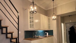 Una cucina moderna con mobili bianchi, una scala in legno e luci a sospensione.