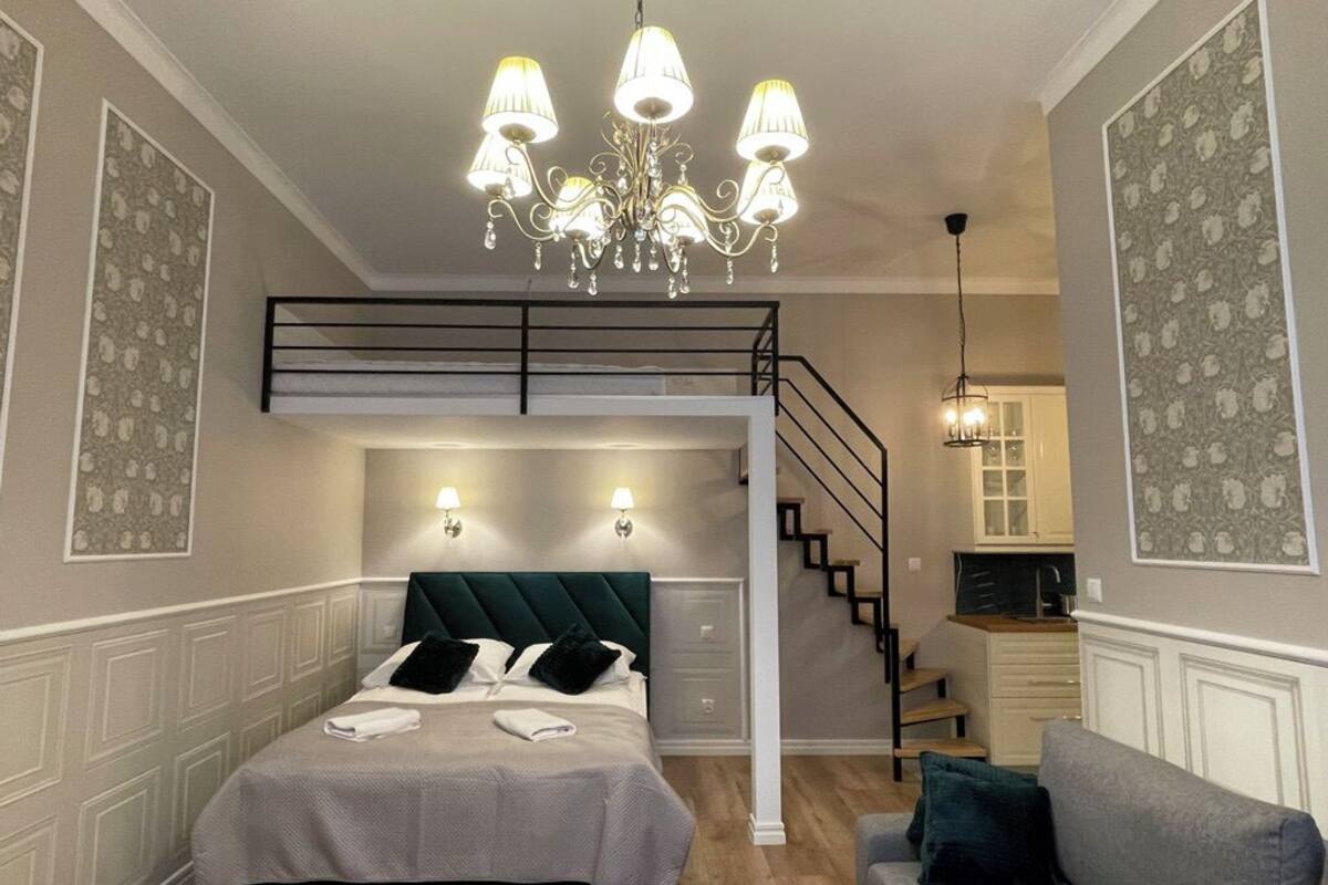 A bedroom with a bunk bed, a staircase, a sofa, and a chandelier.