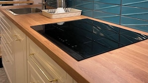 Una cucina con mobili bianchi, piano cottura a induzione nero e parete di fondo rivestita di piastrelle blu.