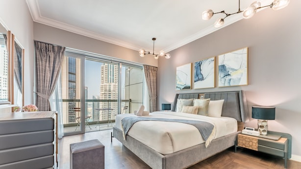 A modern bedroom with a large bed, a desk, and a view of high-rise buildings.
