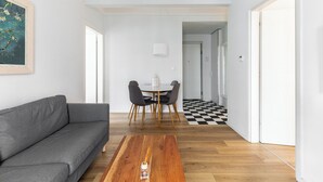 Una sala de estar moderna con un sofá gris, una mesa de centro de madera y una zona de comedor con suelo a cuadros.