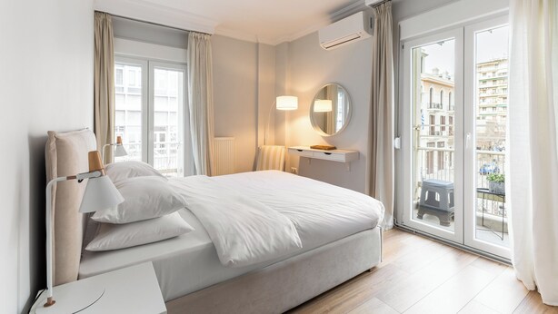 Una habitación de hotel moderna con una cama grande, una mesita de noche, una lámpara, un espejo y vistas a la ciudad a través de una puerta corredera de vidrio.