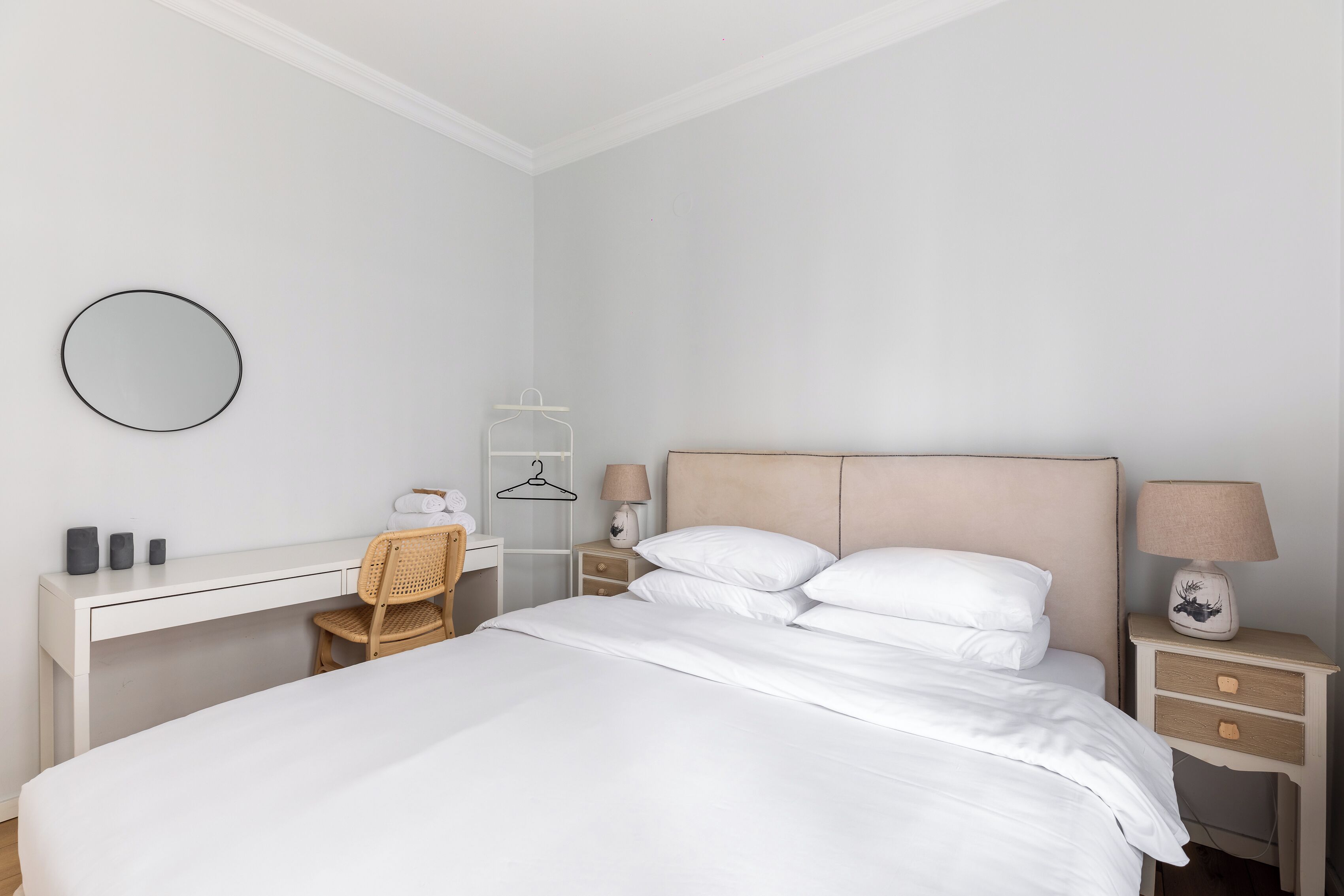 Una camera da letto con un letto, una scrivania, una sedia, un comodino con una lampada e uno specchio fissato al muro.