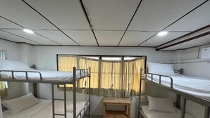 A bunk room with two bunk beds, a small wooden table, and a window with curtains. - Ochatee Hostel (Chiang Mai)