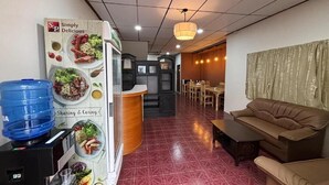 A hotel lobby with a reception desk, a water dispenser, a brown sofa, and a dining area in the background. - Ochatee Hostel (Chiang Mai)