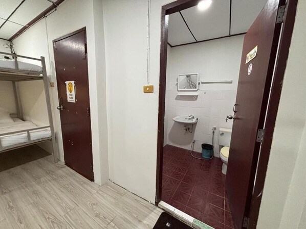 A small, compact bathroom with a single toilet, a sink, and a shower. There is a bunk bed in the adjacent room. - Ochatee Hostel (Chiang Mai)