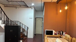 A room with a staircase, a black cabinet, a wooden table with a tissue box, a microwave, and a kettle. - Ochatee Hostel (Chiang Mai)