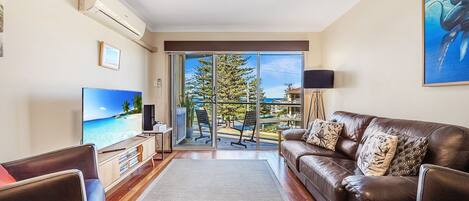 A living room with a leather sofa, a flat-screen TV, and a large window with a view of a tree and buildings.