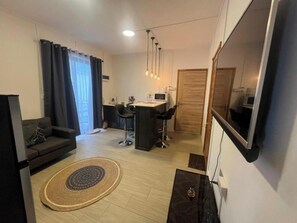A modern living room with a sofa, a coffee table, a dining area with a desk and chairs, and a TV mounted on the wall. - Flic en Flac Paradise Retreat Mauritius (Flic-en-Flac)