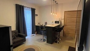 En kompakt opholdsstue med tekøkken, sofa, spiseplads og et fjernsyn ophængt på væggen.