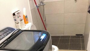 En slank, moderne vaskemaskine i et lille badeværelse med bruseområde.