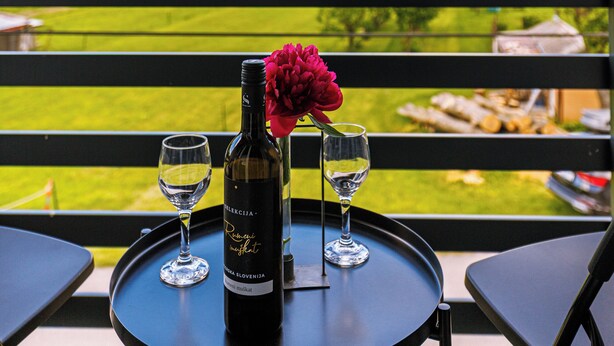 Een tafel met een fles wijn en twee glaasjes op een balkon met uitzicht op een mooi landschap.