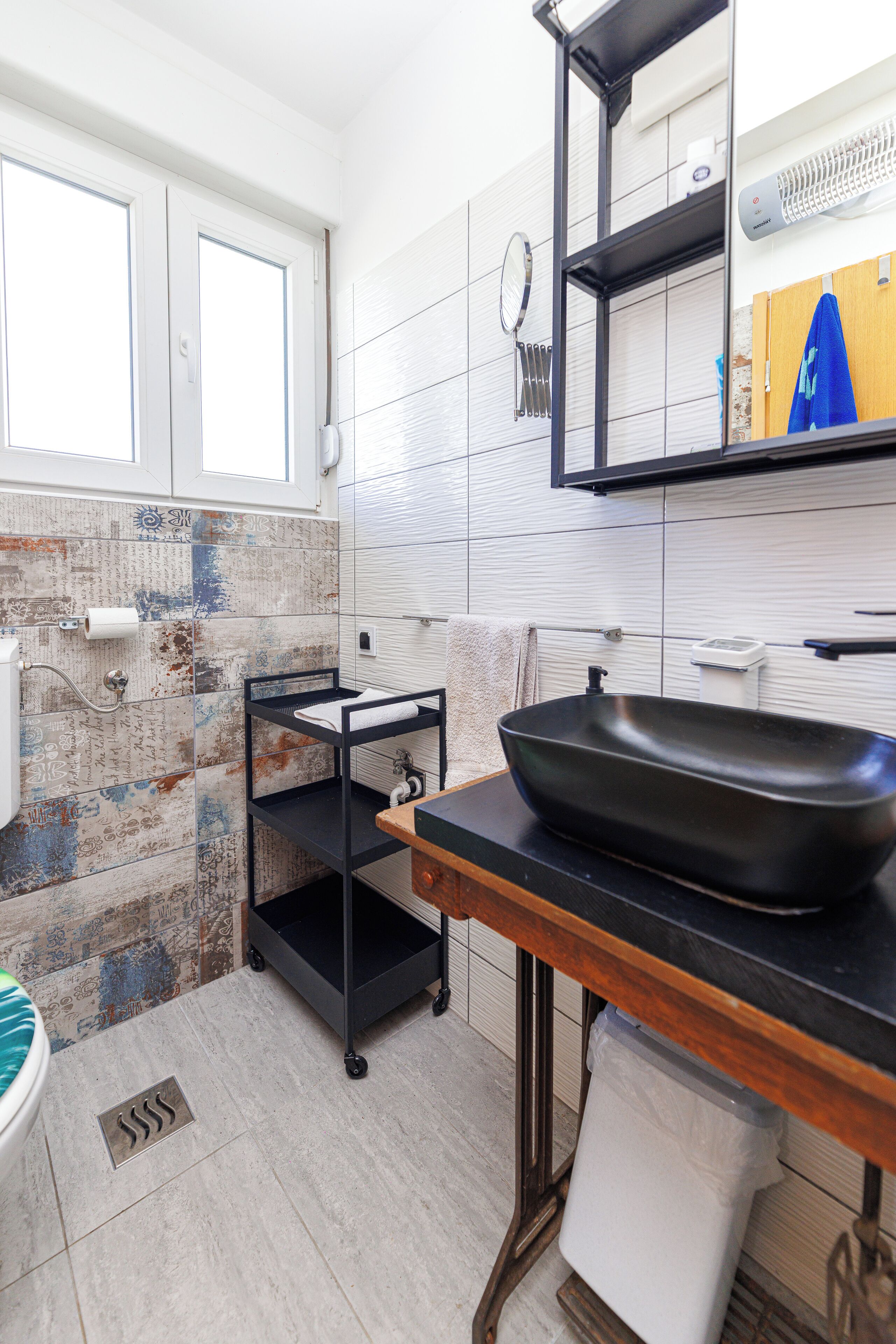 Une salle de bain moderne avec un lavabo noir, un porte-serviettes, un miroir et un espace douche.