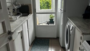 A compact kitchen with a washing machine, a window with a view of greenery, and a potted plant on the windowsill. - A cocoon in Porto .4 to 6 person modular apartment, practical and convivial (Porto)