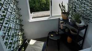 A small room with a large window, a chair, a table, and a shelf with plants. - A cocoon in Porto .4 to 6 person modular apartment, practical and convivial (Porto)