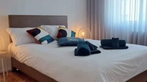 A modern bedroom with a large bed, a hanging light fixture, and a view of the outdoors through sheer curtains. - A cocoon in Porto .4 to 6 person modular apartment, practical and convivial (Porto)