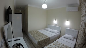 Ein Hotelzimmer mit zwei Einzelbetten, einem kleinen Tisch mit Wasserkocher, einem Spiegel und einer Deckenleuchte.