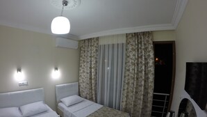 Ein Hotelzimmer mit zwei Betten, einer Deckenleuchte, einer Klimaanlage, einem Fenster mit Vorhängen und einer Kaffeemaschine.